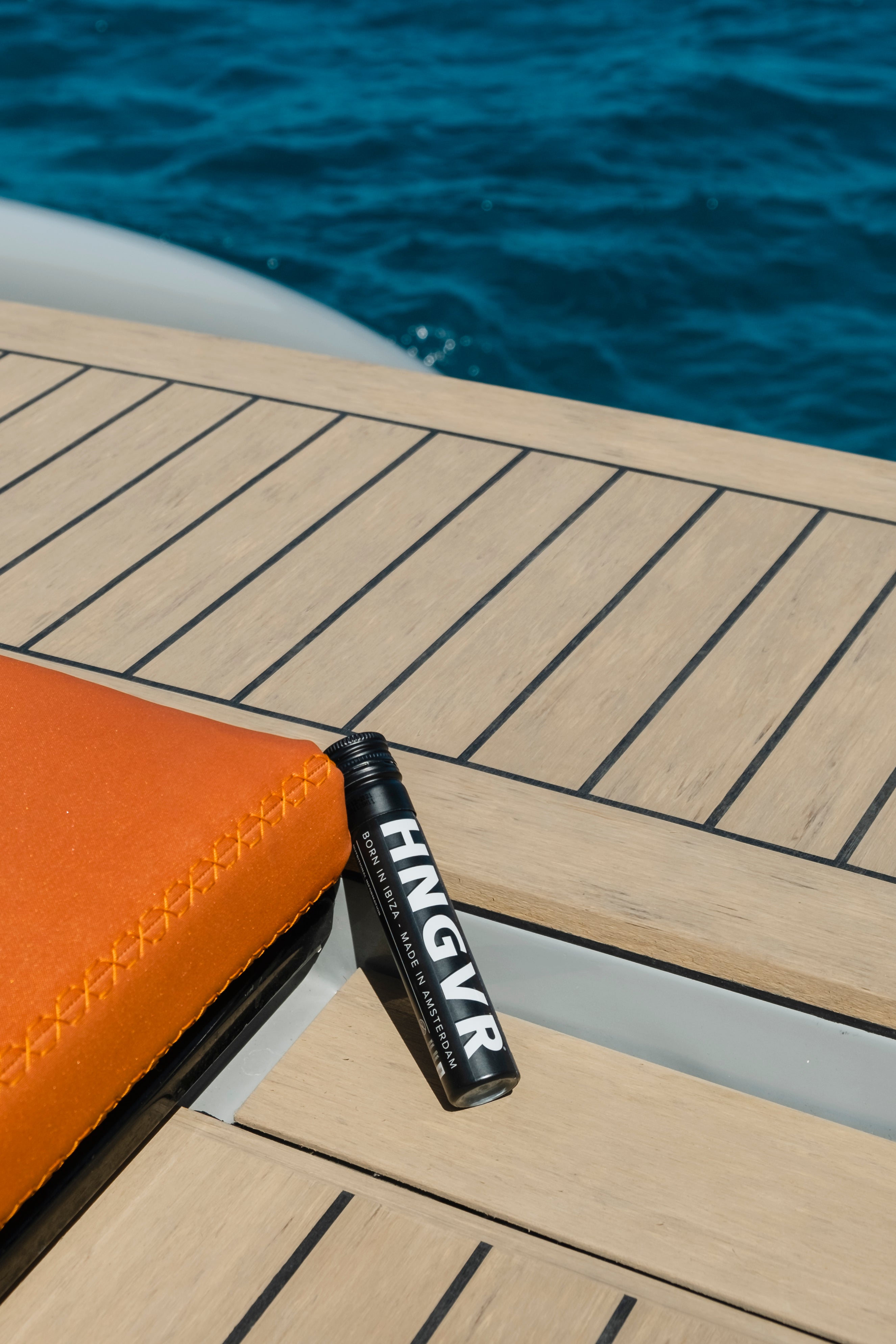Zwarte HNGVR-tube ligt op het houten dek van een boot naast een oranje kussen, met blauw zeewater op de achtergrond.