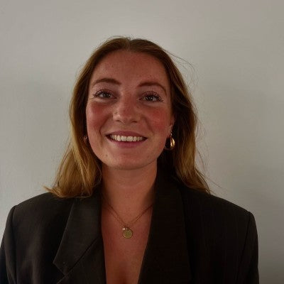  Lachende vrouw met halflang blond haar in een donkere blazer voor een lichte achtergrond. 