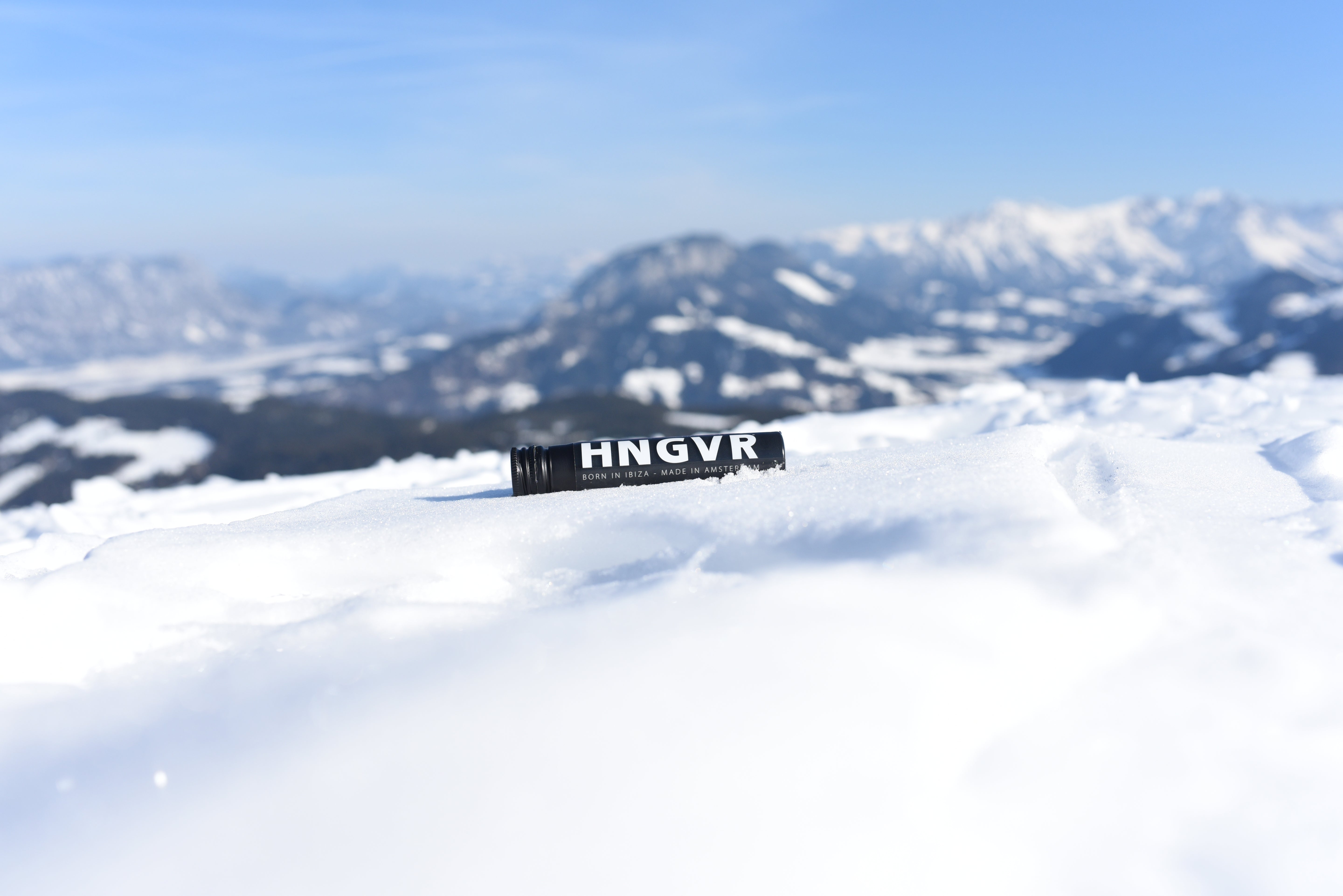 Zwarte HNGVR-tube ligt in de sneeuw op een bergtop, met besneeuwde toppen en een blauwe lucht op de achtergrond.