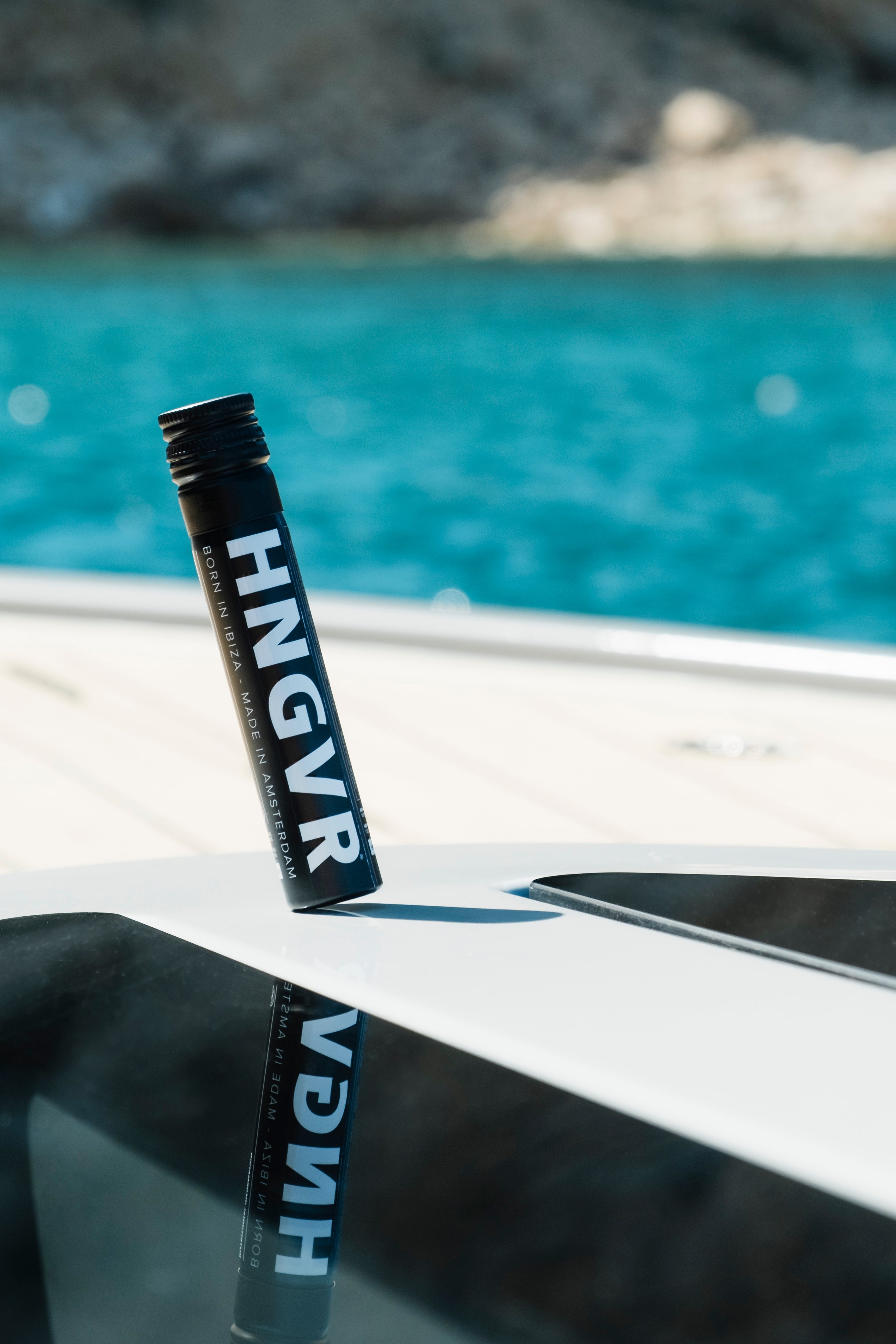 Zwarte HNGVR-tube staat rechtop met spiegeling, tegen een achtergrond van turquoise zeewater en een rotsachtige kust. 