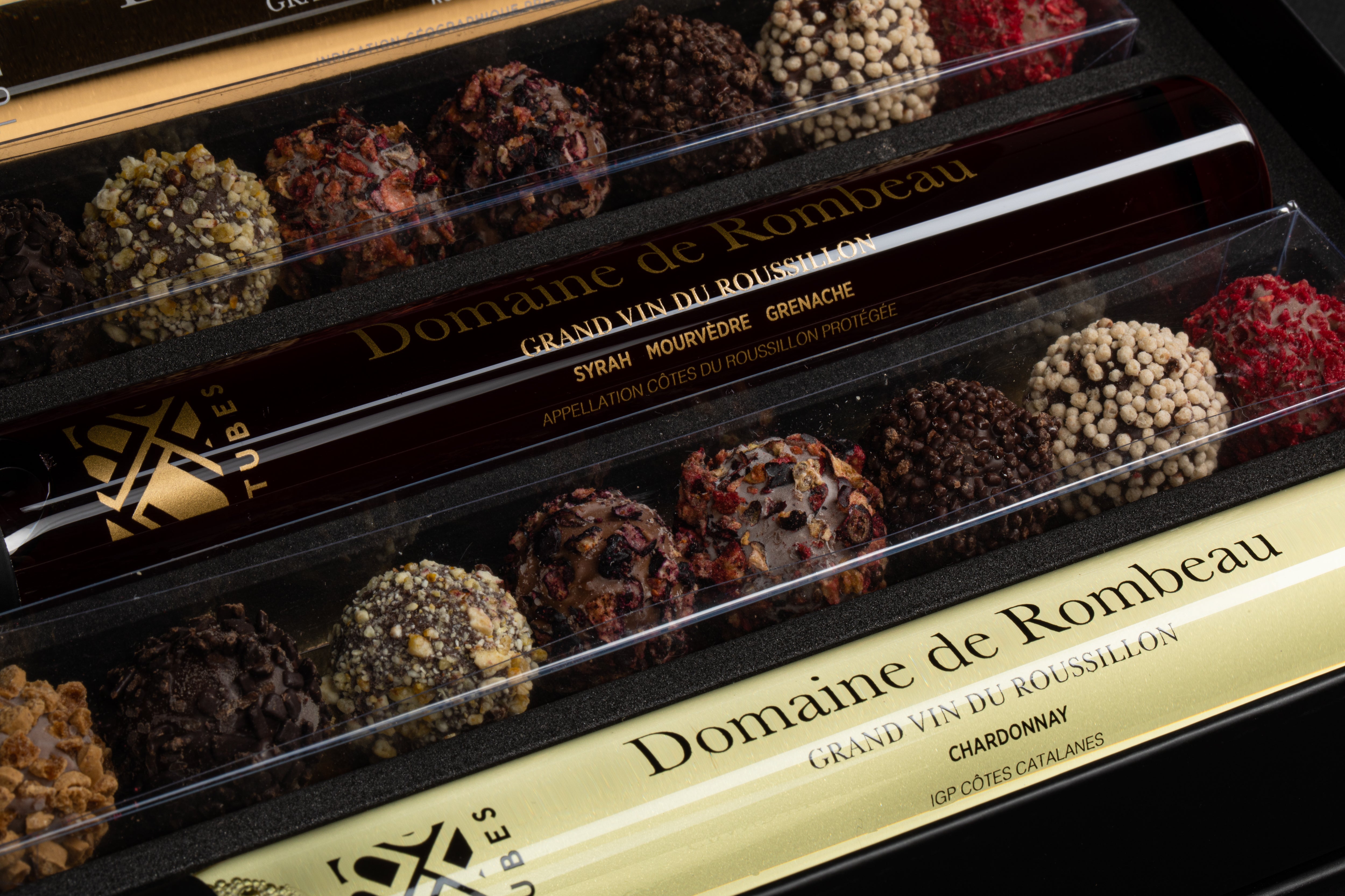 Close-up van een wijn-en-chocoladecadeauset met Domaine de Rombeau Syrah- en Chardonnay-tubes tussen diverse chocoladetruffels.